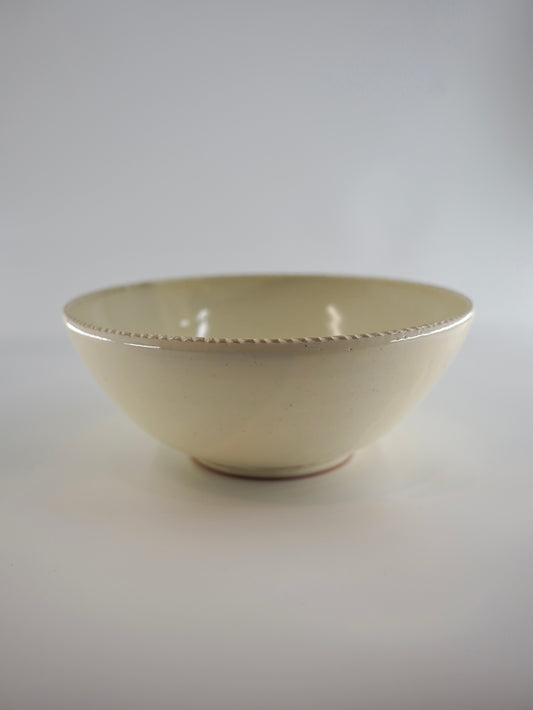 A small cream-colored ceramic bowl with a subtle textured rim, photographed against a neutral light gray background.