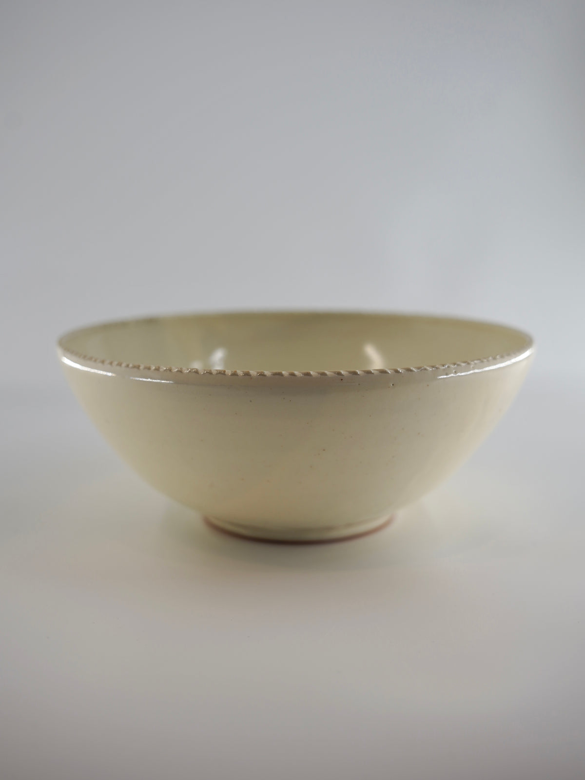 A cream-colored ceramic bowl with a subtle textured rim, photographed against a neutral light gray background.