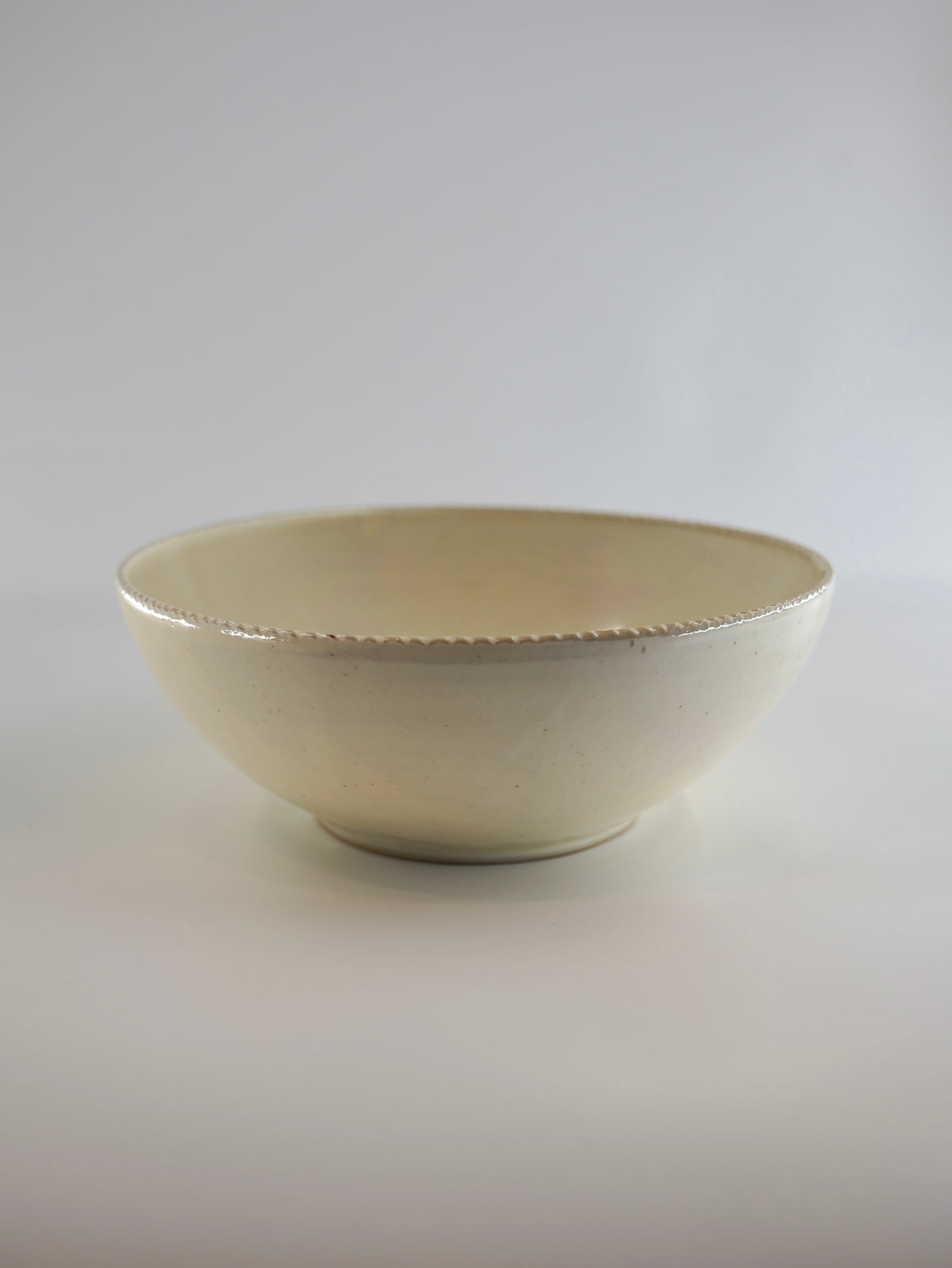 A small ceramic bowl with a cream-colored glaze and a subtle textured rim, photographed against a neutral light gray background.