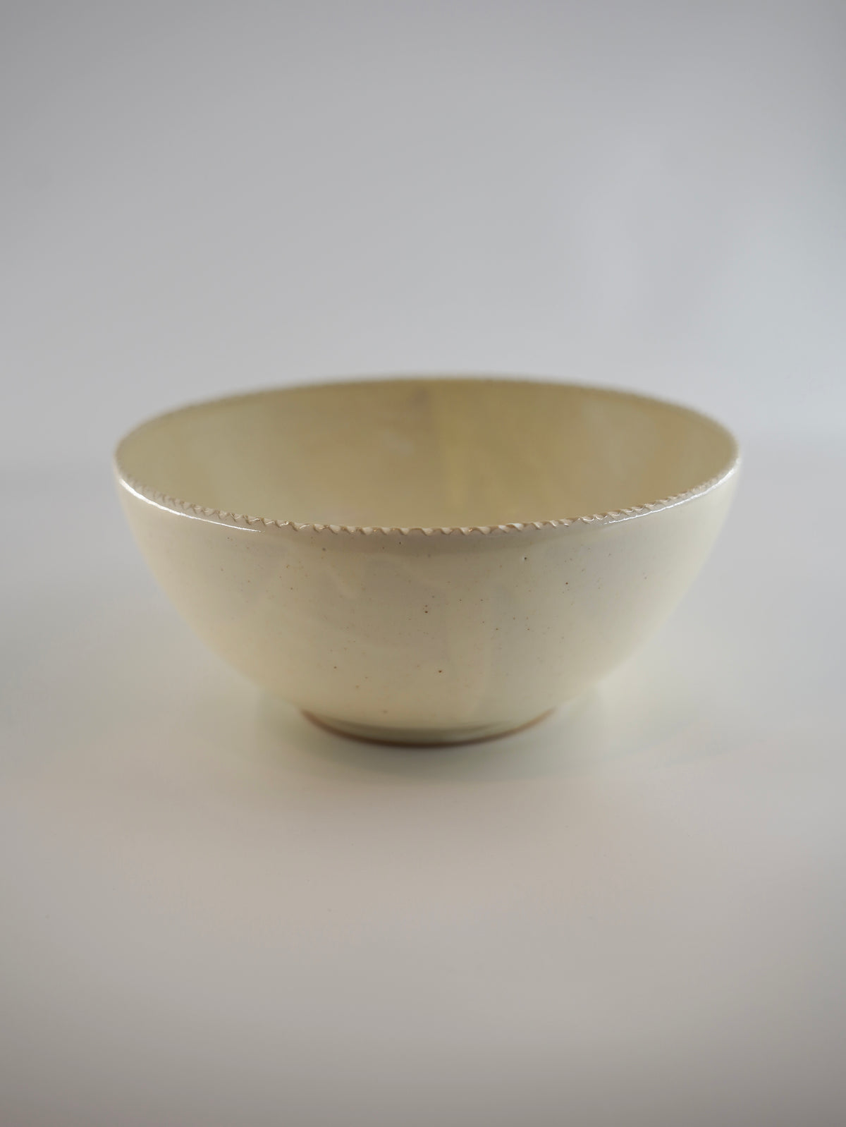 A small ceramic bowl with a cream-colored glaze and a delicate wavy rim, photographed against a neutral light gray background.