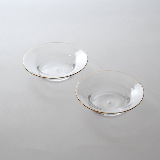 Two clear glass dishes with golden rims on a light background, one nested inside the other.