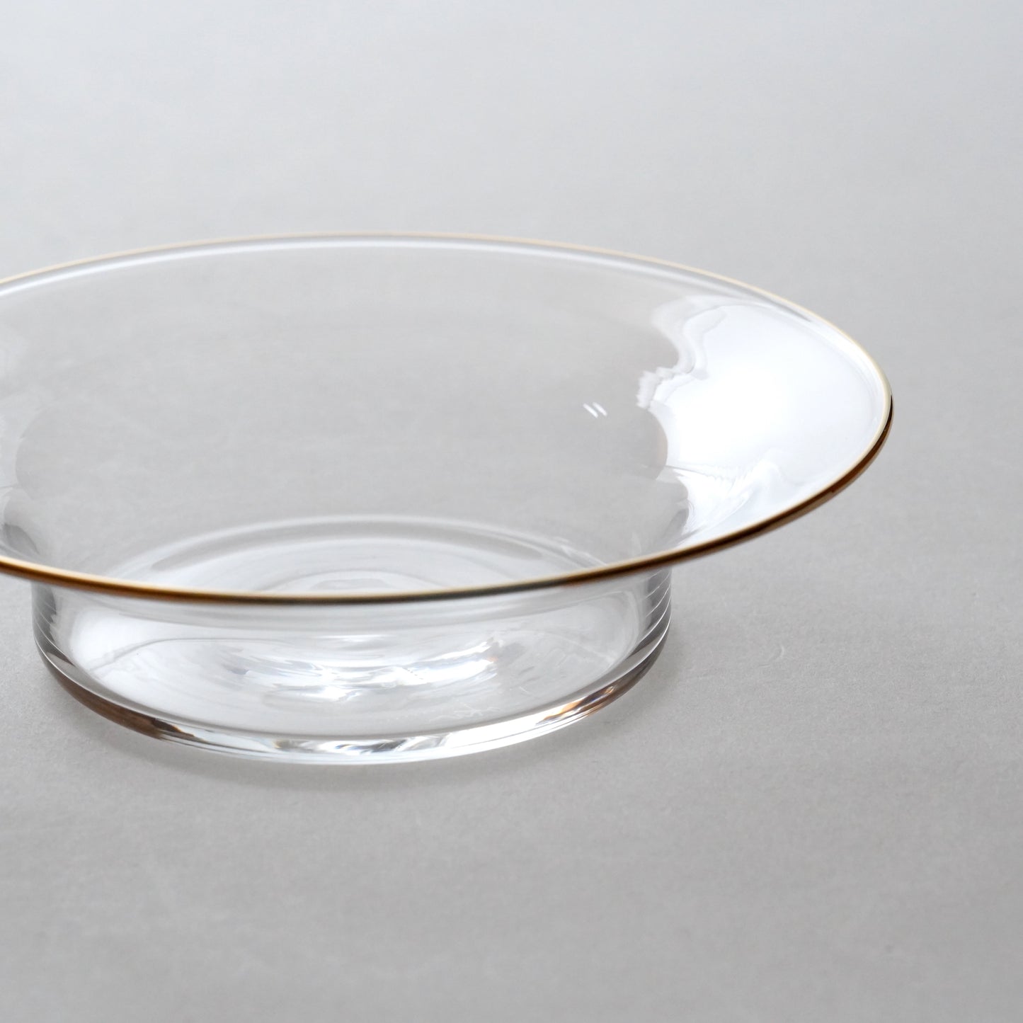 Clear glass bowl with gold rim on a neutral background