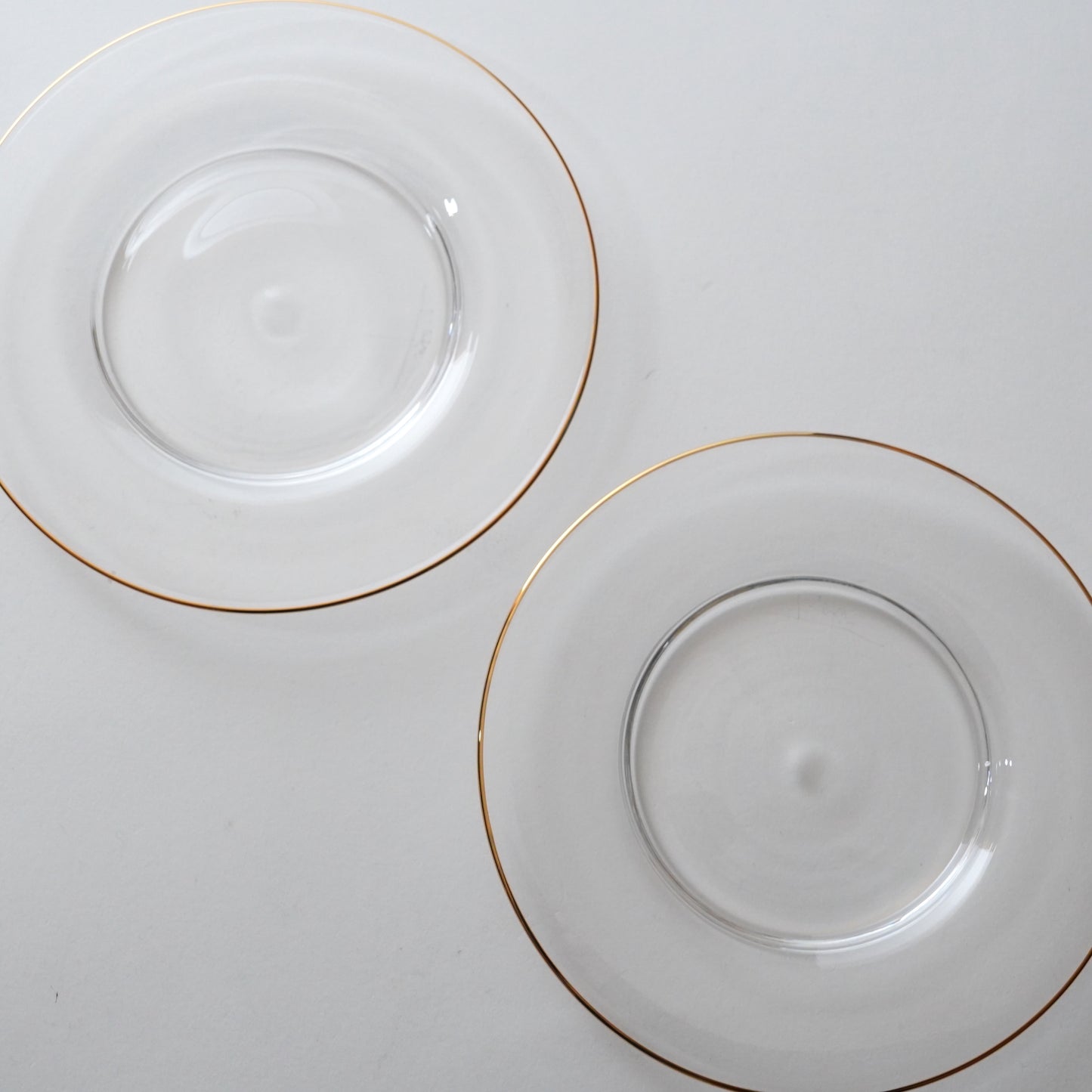 Two clear glass plates with gold rims on a white background