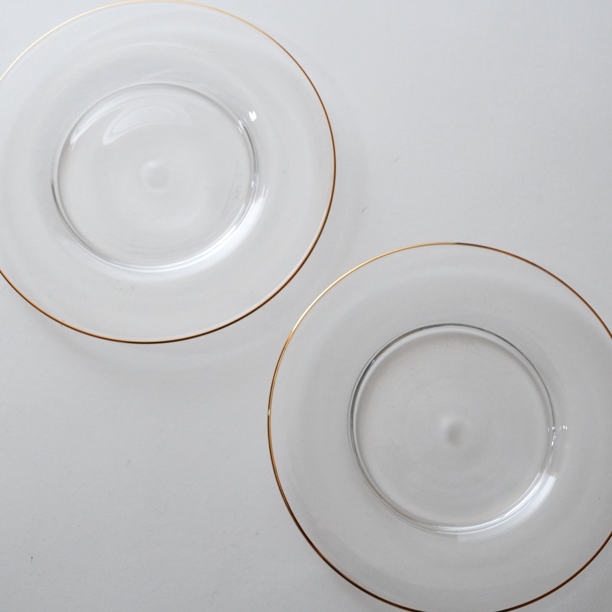 Two clear glass plates with gold rims on a white background