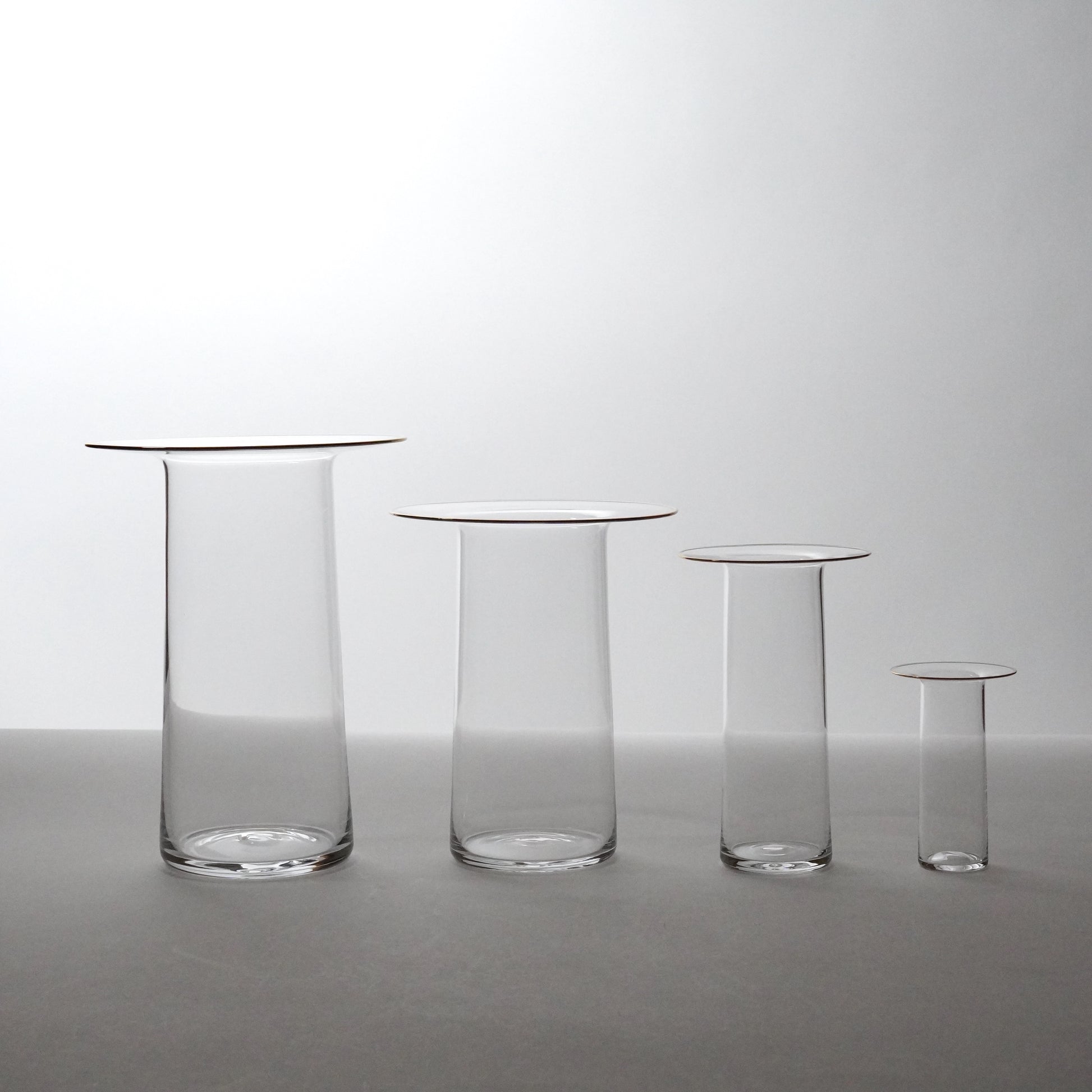 Set of four clear glass vases of different sizes on a gray background