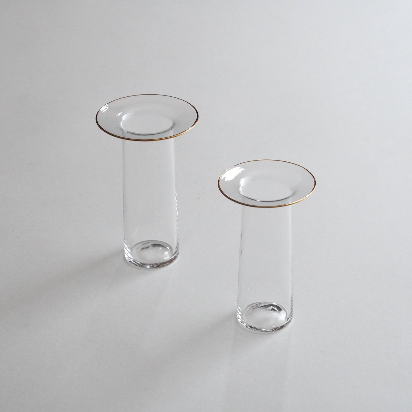 Two clear glass vases with golden rims, one larger and one smaller, placed on a grey surface.
