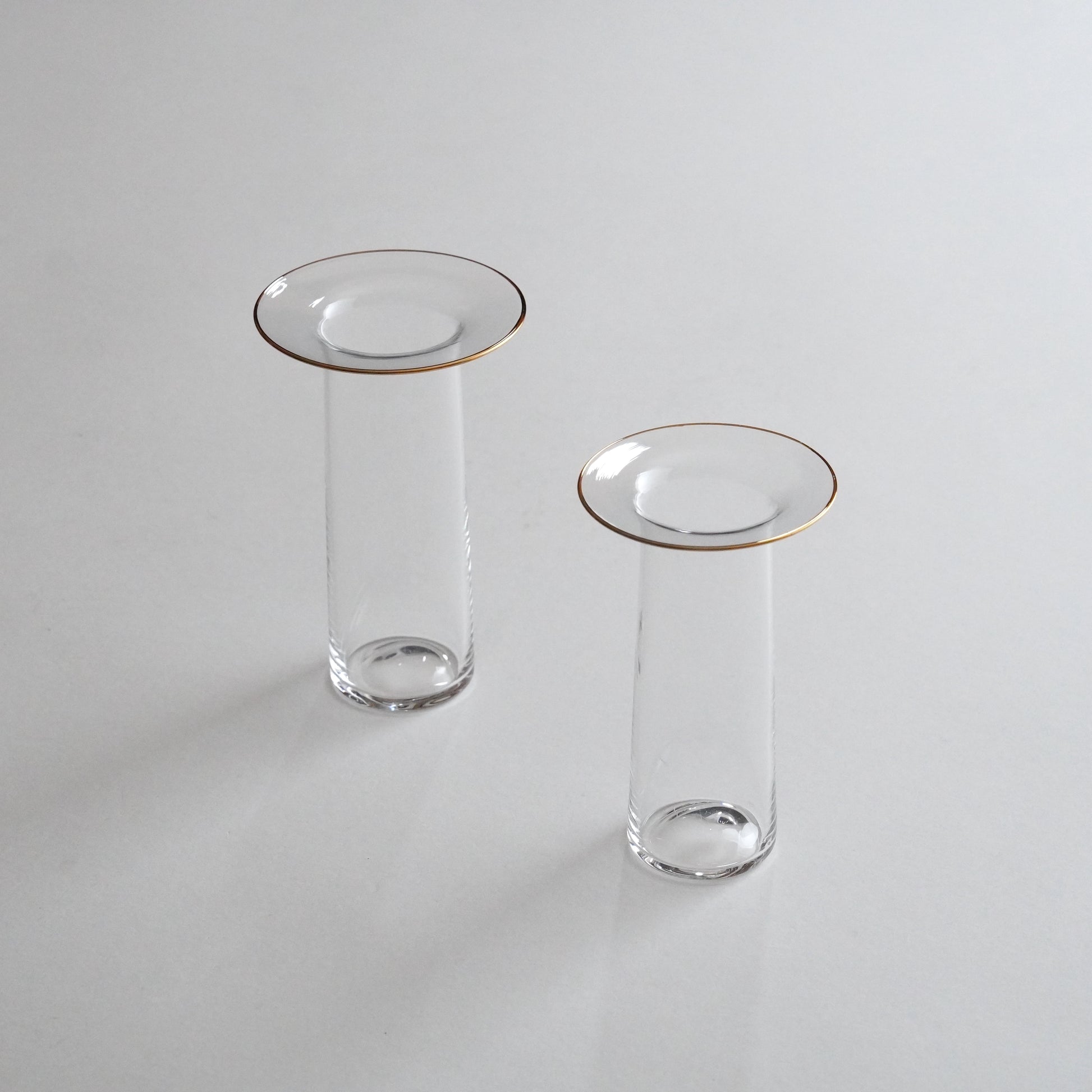 Two clear glass vases with golden rims, one larger and one smaller, placed on a grey surface.