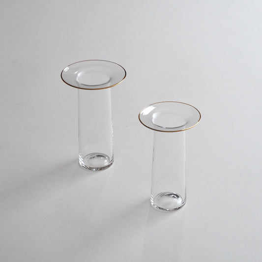 Two clear glass vases with golden rims, one larger and one smaller, placed on a grey surface.