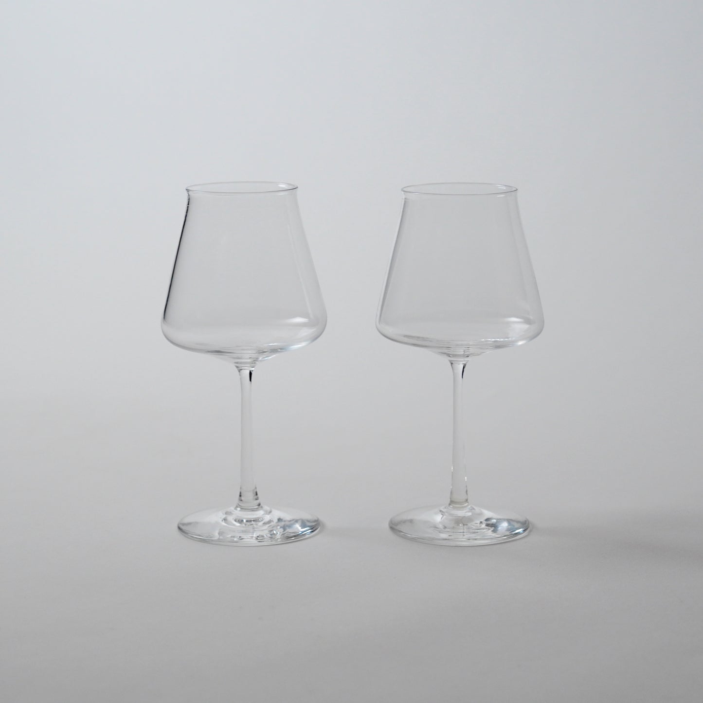 Two clear glass wine glasses with a wide bowl and a stem, displayed against a neutral background.