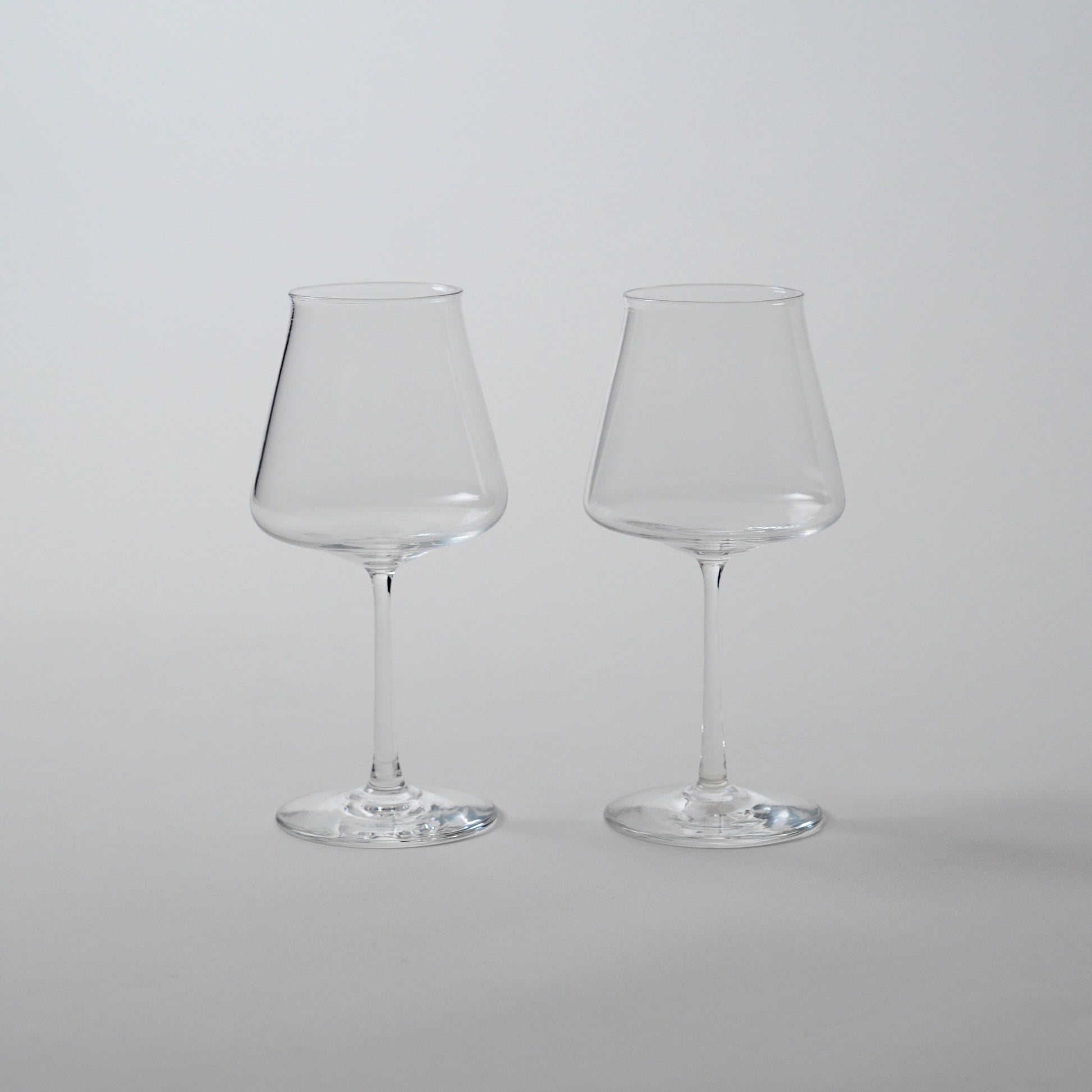 Two clear glass wine glasses with a wide bowl and a stem, displayed against a neutral background.