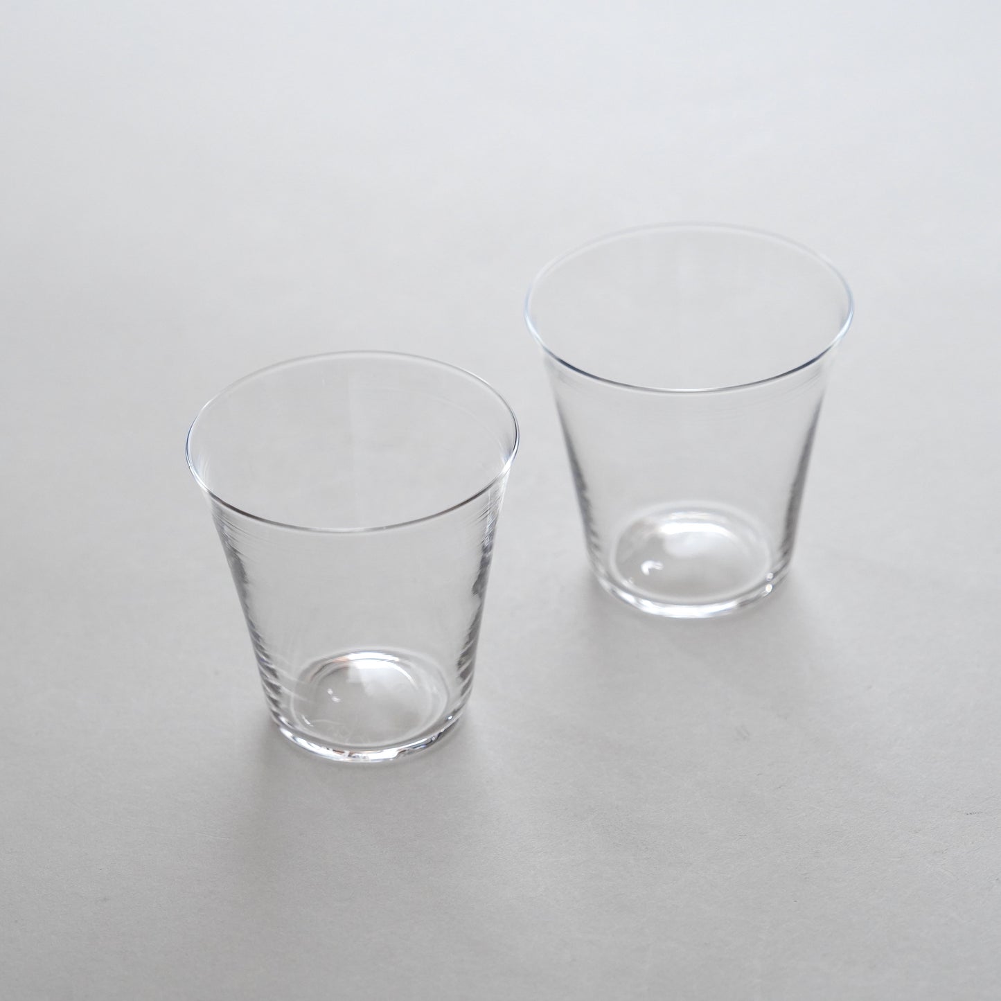 Two clear glass water glasses placed side by side on a grey surface.