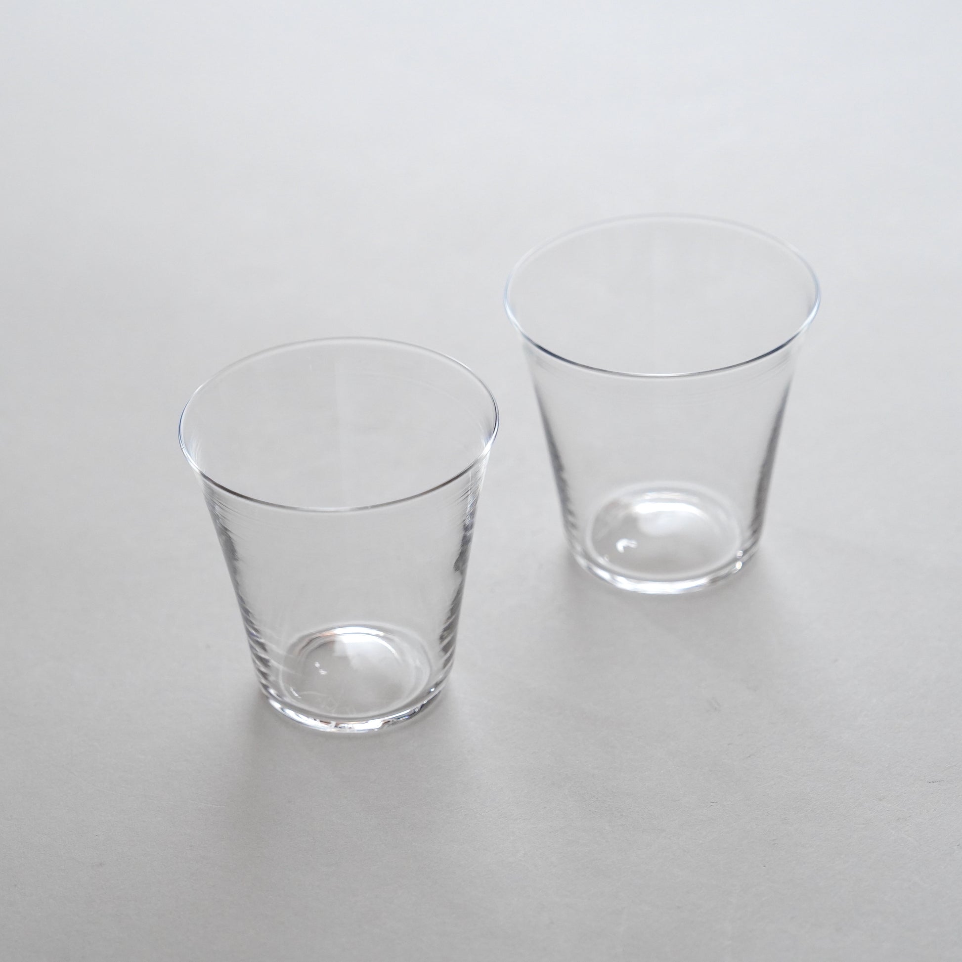 Two clear glass water glasses placed side by side on a grey surface.