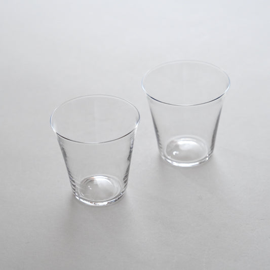Two clear glass water glasses placed side by side on a grey surface.
